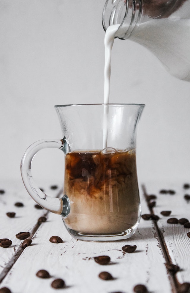 Milch wird aus eine Kanne in den Kaffee geschüttet.